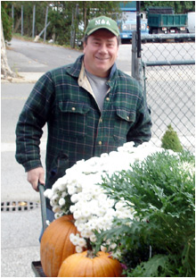 A crew member in an M&A cap wheeling white mums and pumpkins at the yard